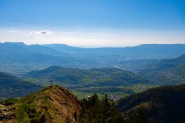 Au sommet de la Galoppaz, une croix domine le village de Curienne au second plan et Chambery à l'arrière plan.