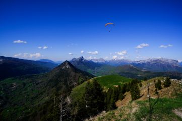 Vue du massif des Bauges depuis la Galoppaz, un parapentiste occupant le ciel au premier plan